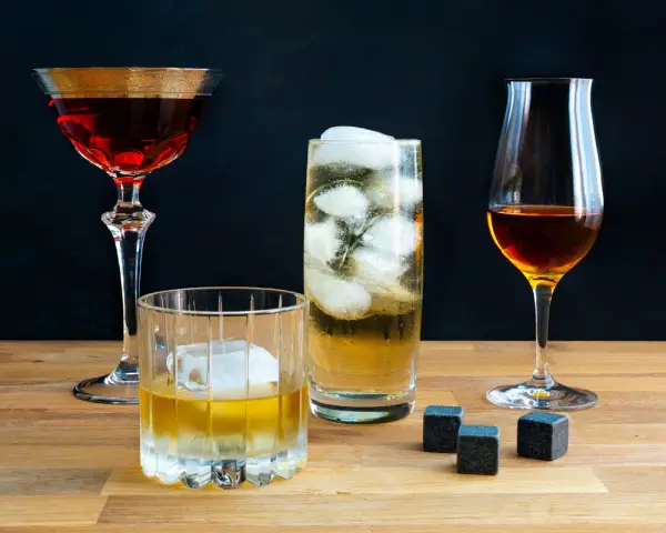 Vier Gläser mit verschiedenen Getränken, darunter ein Whisky-Cocktail, ein Highball und ein Nosing-Glas. So trinkt man Whisky: pur, mit Eis oder als Mixgetränk.