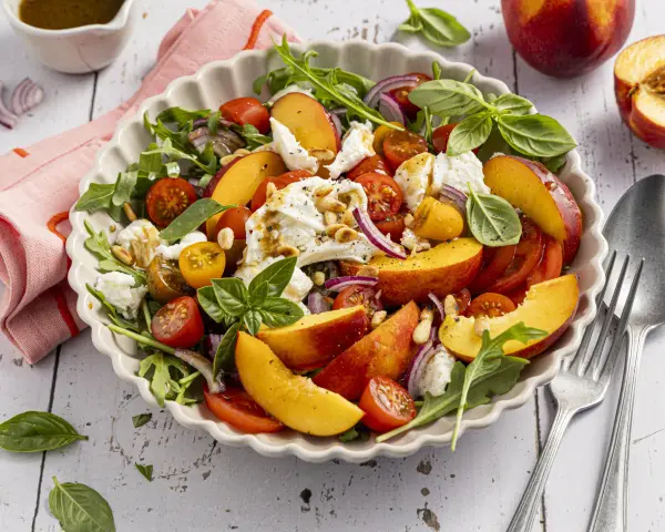 Erfrischender Salat mit saftigen Nektarinen, Tomaten, Mozzarella und Rucola, beträufelt mit Balsamico-Dressing.