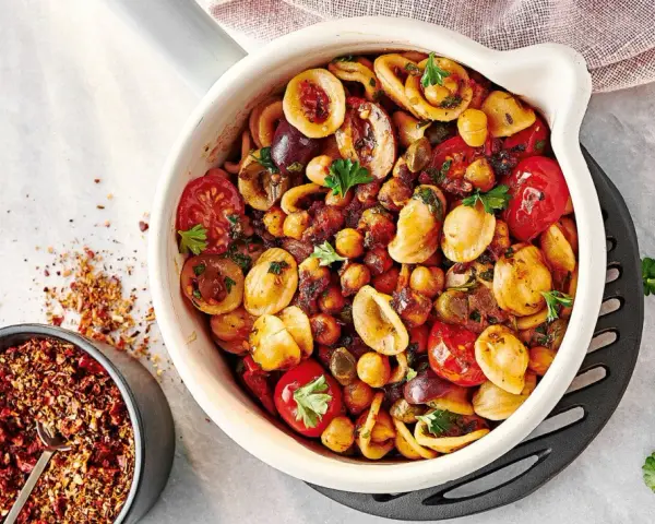 Ein bunter Nudelsalat mal anders: Orecchiette mit Kichererbsen, Kirschtomaten, Oliven und Kräutern in einer Auflaufform. Daneben eine Schale mit Gewürzmischung.