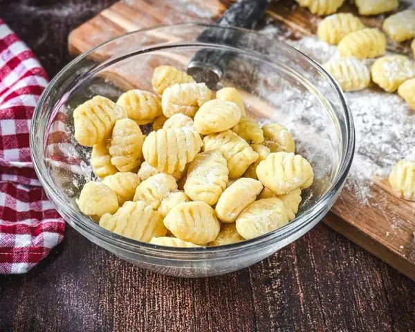 Frisch gemachte Gnocchi in einer Schüssel, bereit zum Kochen. Auf dem Holzbrett liegen weitere Gnocchi, die zeigen, wie einfach es ist, Gnocchi selber machen.
