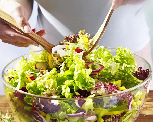 Frischer gemischter Salat mit knackigem Salat, Radieschen, Zwiebeln und Pilzen wird mit Holzsalatbesteck vermischt.