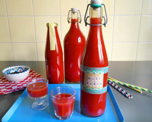 Rot gefüllte Flaschen mit dem Aufdruck "Mexikaner Rezept" und kleine Gläser mit dem Getränk.