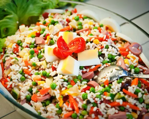 Reissalat mit Erbsen, Karotten, Ei und Wurst – ein gesunder Salat zum Grillen, garniert mit Tomaten und Salatblättern.