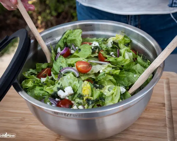 Frischer Salat zum Grillen, zubereitet von Landfrauen. Knackiger Salat mit Tomaten, Zwiebeln und Feta in einer Edelstahlschüssel.