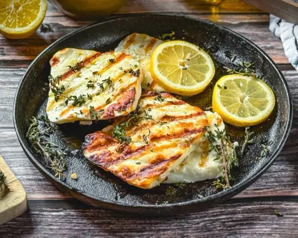 Perfekt gegrillter Halloumi mit Kräutern und Zitronenspalten auf einer Gusseisenplatte. Ein Genuss für alle Sinne!