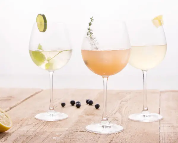 Drei elegante Gläser mit erfrischenden champagner cocktails, garniert mit Limette, Kräutern und Zitrone, stehen auf einem Holztisch.