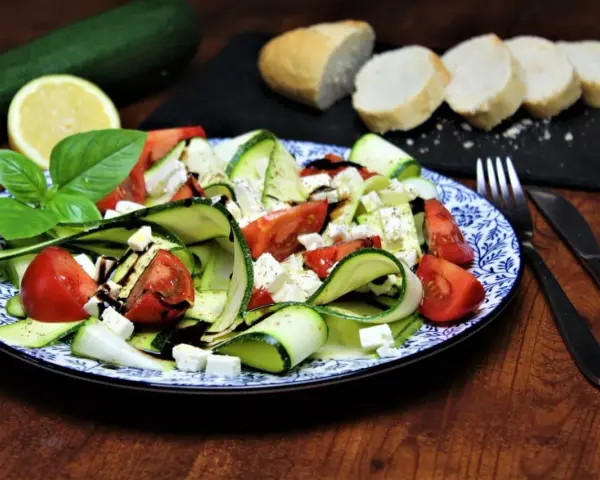Ein erfrischender, sommerlicher Zucchini-Salat mit Tomaten und Feta, garniert mit Basilikum und Balsamico. Dazu Baguettescheiben.
