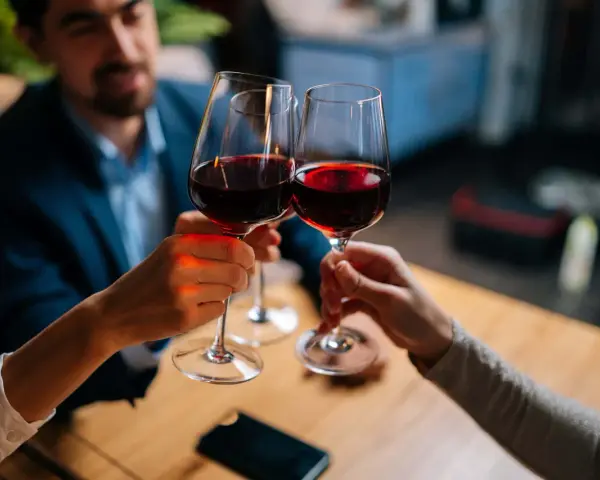 Drei Personen stoßen mit Rotwein an. Sie halten das weinglas richtig, am Stiel, um die Temperatur des Weins zu bewahren.