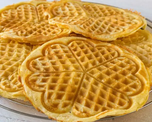 Goldbraune Herz-Waffeln, frisch gebacken aus waffelteig ohne butter, liegen auf einem Gitter.