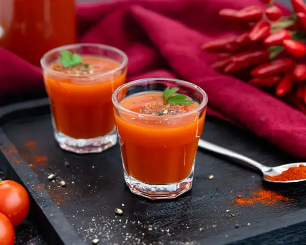 Zwei Gläser würziger mexikanischer Tomatensaft, garniert mit Petersilie, neben frischen Tomaten und Chilis.