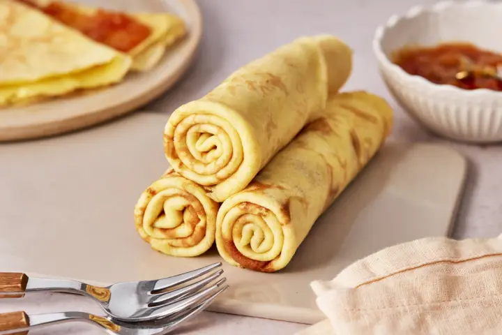 Gestapelte Quark Pfannkuchen, goldbraun gebacken, mit einer Schale Marmelade und Gabeln daneben.
