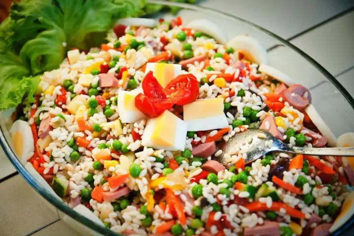 Reissalat mit Erbsen, Karotten, Ei und Wurst – ein gesunder Salat zum Grillen, garniert mit Tomaten und Salatblättern.