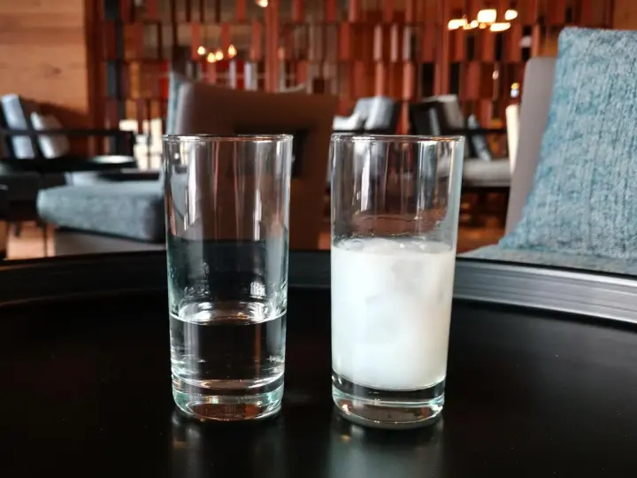 Zwei Gläser auf einem Tisch: eines mit klarem Wasser, das andere mit milchigem Ouzo. Ein Vergleich zwischen Raki und Ouzo.