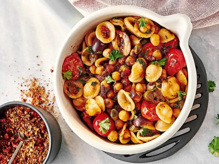 Ein bunter Nudelsalat mal anders: Orecchiette mit Kichererbsen, Kirschtomaten, Oliven und Kräutern in einer Auflaufform. Daneben eine Schale mit Gewürzmischung.