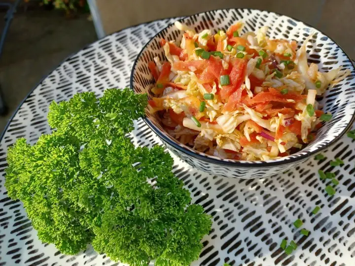 Frischer Chinakohlsalat mit Honig-Senf Dressing, garniert mit Lachs und Schnittlauch. Daneben ein Bund glatte Petersilie.