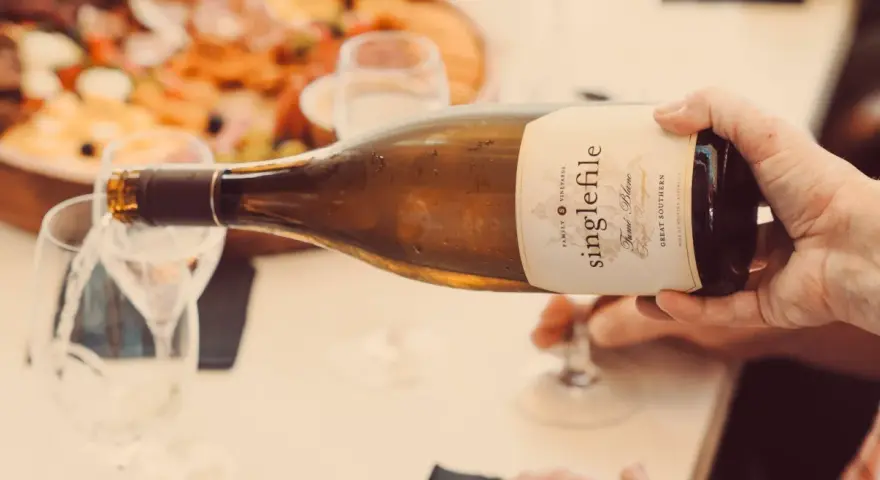 Eine Hand gießt einen **fumé wein** aus einer Flasche in ein Glas. Im Hintergrund ist eine Platte mit Speisen zu sehen.
