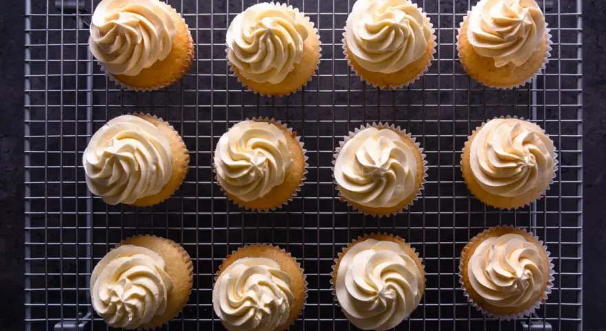 Zwölf Cupcakes mit cremiger deutscher Buttercreme auf einem Gitter.