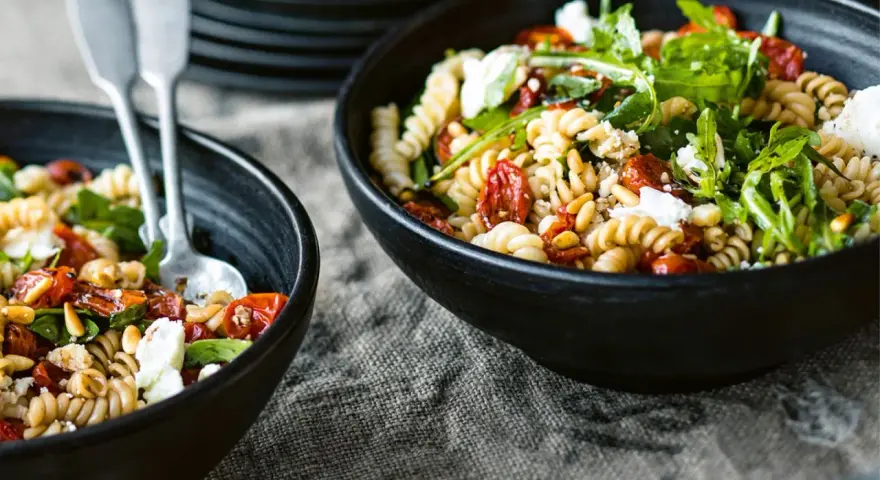 Zwei Schüsseln mit Nudelsalat, perfekt für das Grillen. Fusilli mit getrockneten Tomaten, Rucola und Feta.