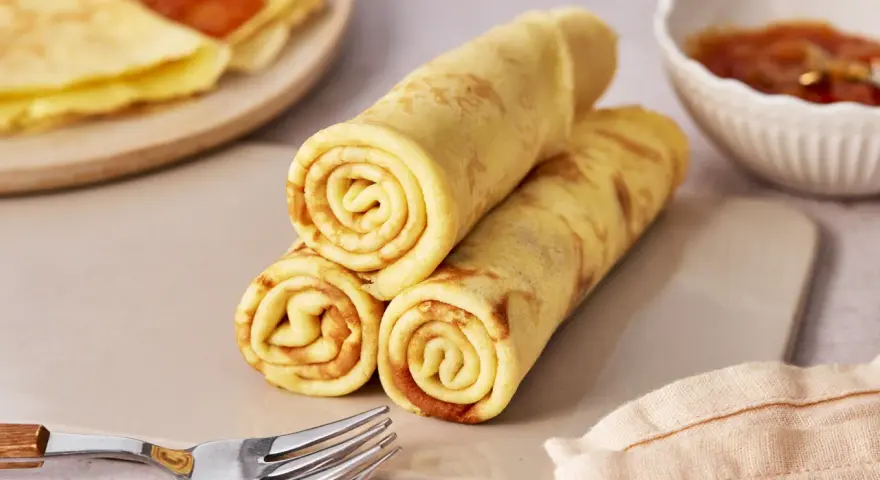 Gestapelte Quark Pfannkuchen, goldbraun gebacken, mit einer Schale Marmelade und Gabeln daneben.