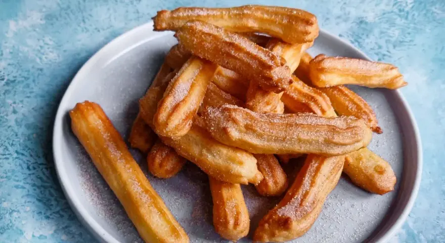 Goldbraune Churros, frisch aus dem Airfryer, mit Zucker bestreut auf einem grauen Teller.