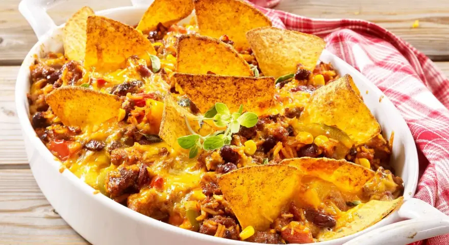 Herzhafter nacho auflauf mit Hackfleisch, Bohnen, Mais und geschmolzenem Käse, garniert mit Tortilla-Chips und frischen Kräutern.