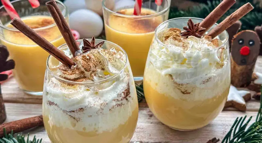Festliche Gläser mit cremigem Eggnog, garniert mit Zimtstangen und Schlagsahne. Das perfekte Eggnog Rezept original für Weihnachten.