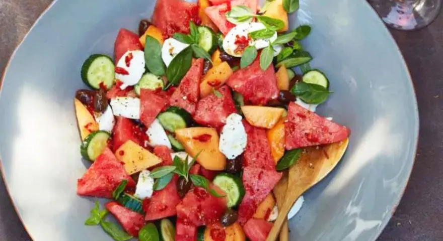 Erfrischender Melonensalat mit Mozzarella, Gurke und Basilikum auf einem grauen Teller.