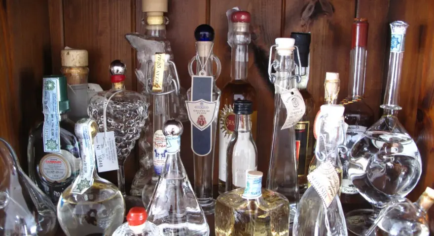 Regal voller Grappa-Flaschen, einige mit Etiketten, die den **Grappa Prozent** angeben.