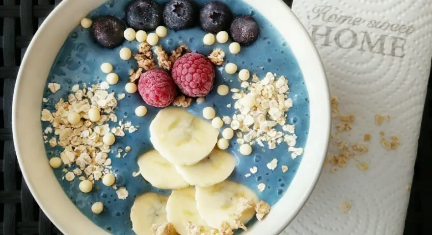 Blauer Smoothie-Bowl mit Blaubeeren, Himbeeren, Bananenscheiben und Granola. Perfekt für gesunde smoothie rezepte.