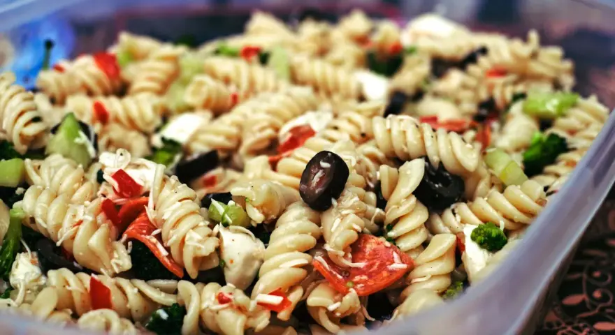 Nudelsalat mit Spiralnudeln, Oliven, Paprika und Brokkoli in einer Plastikschüssel.