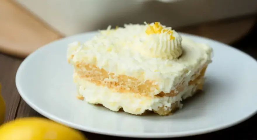Ein Stück cremiges Limoncello Tiramisu, garniert mit Zitronenzesten und einem Tupfer Sahne, auf einem weißen Teller.