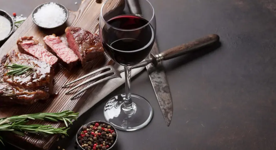 Ein saftiges Steak, perfekt zubereitet, mit einem Glas Rotwein. Was ist Malbec? Ein vollmundiger Wein, der dieses Gericht abrundet.