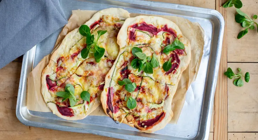 Zwei Flammkuchen mit Zucchini und Roter Bete, garniert mit frischen Blättern. Eine histaminarme Alternative, bei der man auf Weintrauben verzichtet.