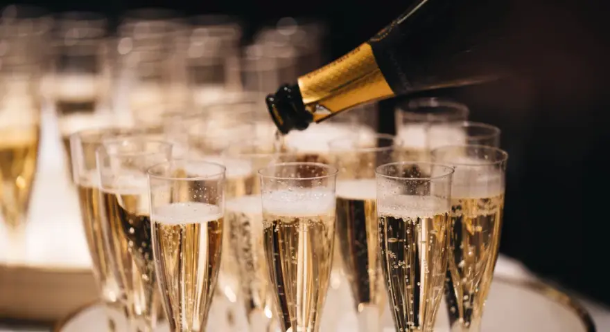 Sekt wird in Gläser gefüllt, die auf einem Tablett stehen. Die Bläschen steigen auf und erinnern daran, woher Champagner kommt.