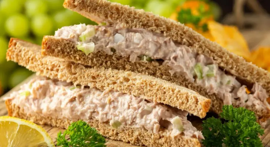Zwei Tramezzini mit Thunfischsalat, Sellerie und Zwiebeln auf Vollkorntoast. Dazu Trauben, Zitrone und Petersilie. Perfekt für schnelle Tramezzini Rezepte.