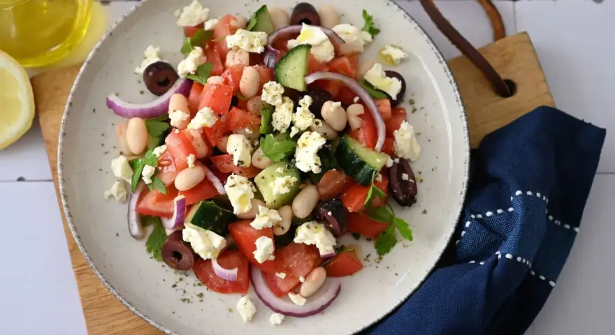 Frischer griechischer Bohnensalat mit Tomaten, Gurken, roten Zwiebeln, Oliven und Feta. Ein Spritzer Olivenöl und Zitrone machen ihn perfekt.