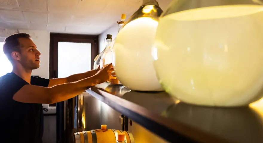 Mann sortiert Flaschen für die Gin-Lagerung. Daneben stehen Fässer und große Glasballons.