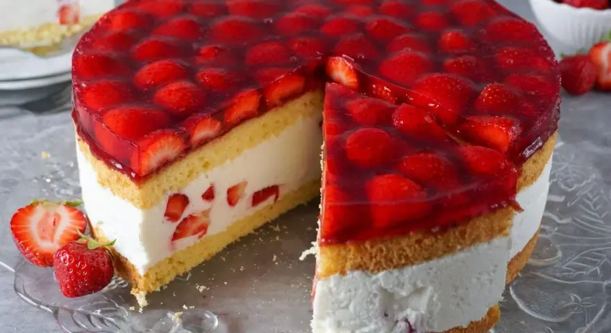 Eine **einfache Torte** mit Biskuit, Sahne und vielen frischen Erdbeeren unter rotem Tortenguss. Ein Stück ist bereits angeschnitten.