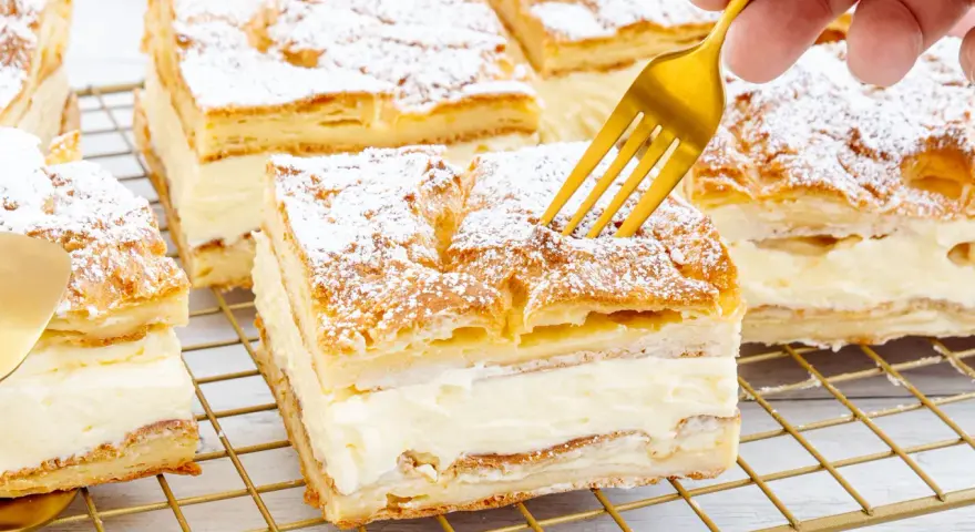 Ein goldener Löffel sticht in ein Stück polnischer Puddingkuchen, bestäubt mit Puderzucker.