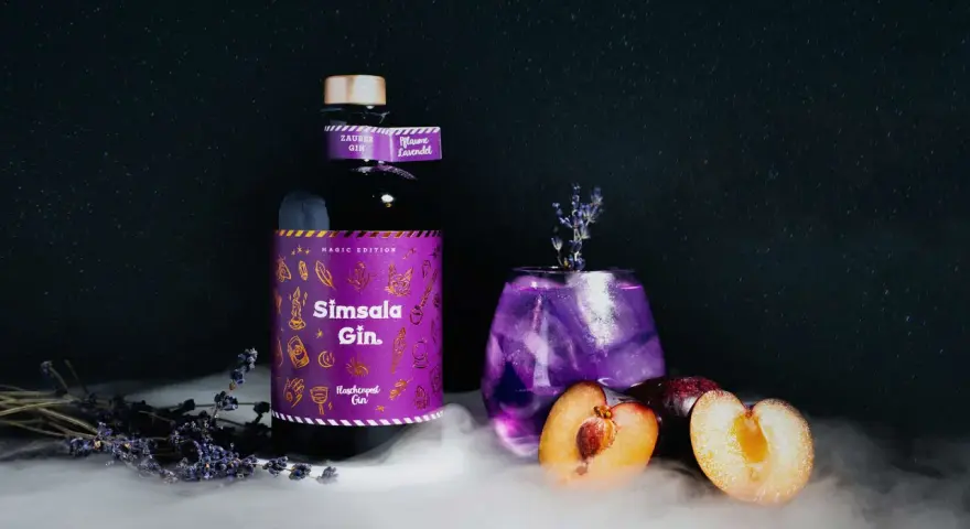 Ein magischer lila Gin Tonic mit Pflaume und Lavendel, daneben eine Flasche Sîmsala Gin.