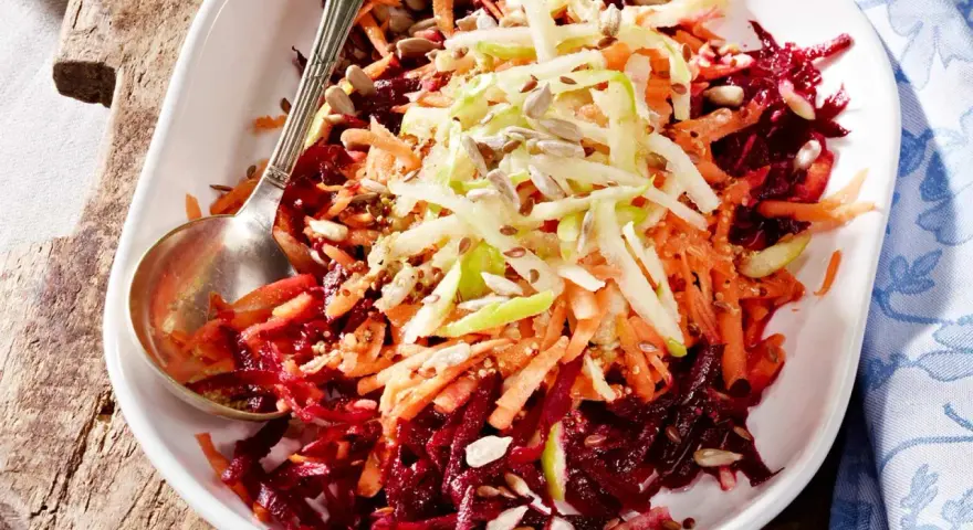 Bunter Salat aus geriebener roter Bete, Karotten und Apfelstiften, garniert mit Sonnenblumenkernen.
