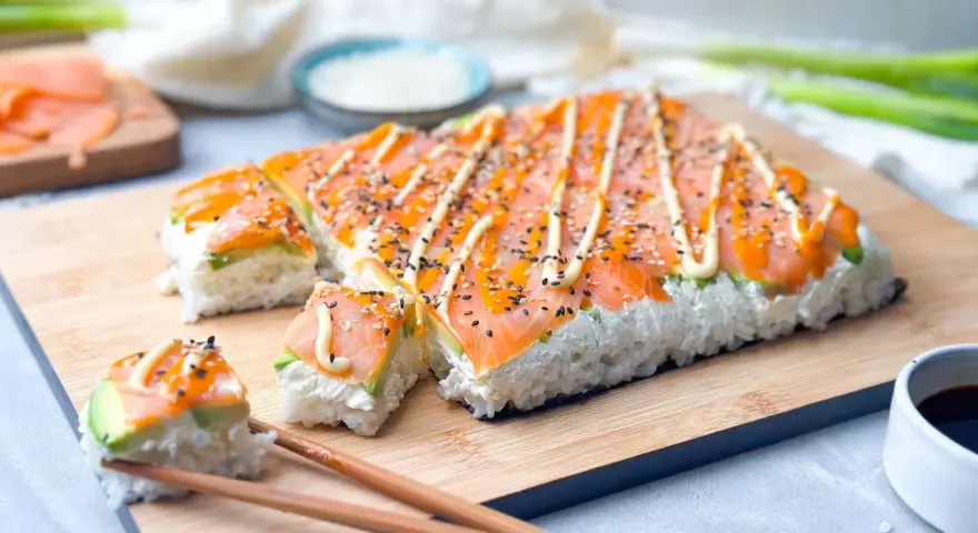 Rechteckiges Sushi mit Lachs und Avocado, verziert mit Mayonnaise und Sesam. Perfekt, um Sushi selber machen zu lernen!