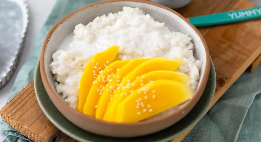 Schüssel mit cremigem **sticky rice** und saftigen Mangoscheiben, bestreut mit Sesam. Ein köstlicher Genuss!