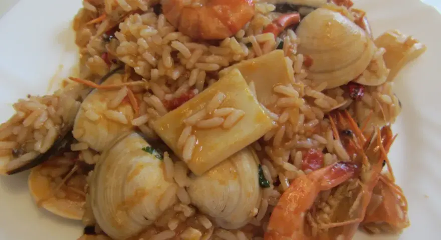 Ein köstlicher arroz de marisco mit Garnelen, Muscheln und Tintenfischstücken, serviert auf einem weißen Teller.