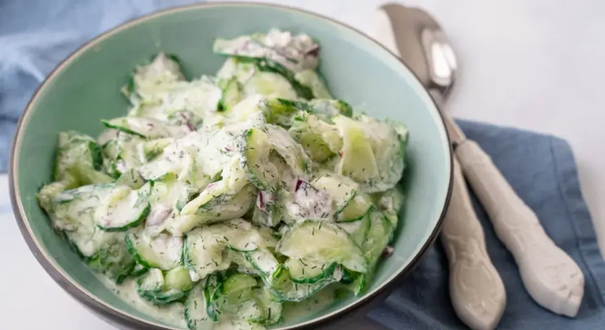 Frischer gurkensalat mit saurer sahne und Dill, garniert mit roten Zwiebeln, in einer Schüssel serviert.