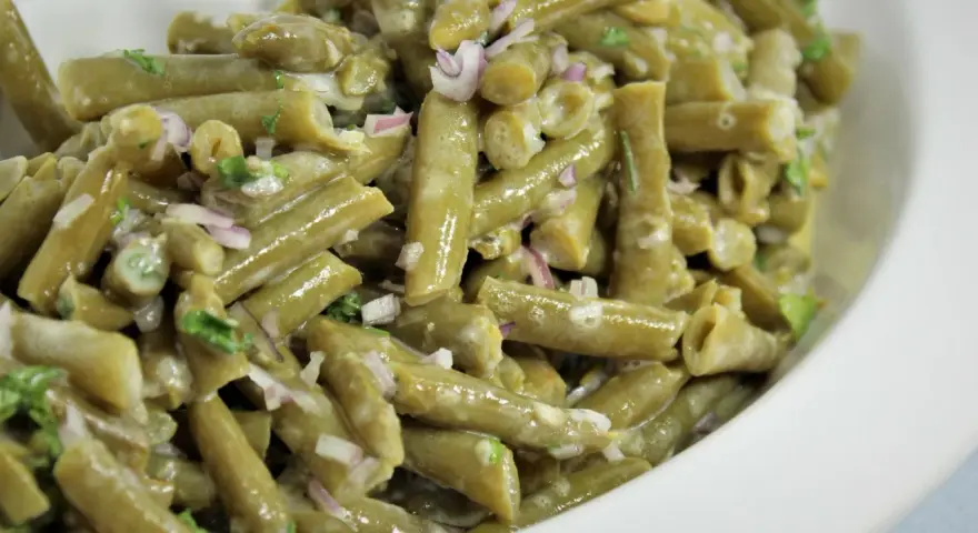 Grüner Bohnensalat mit cremigem Dressing, roten Zwiebeln und Kräutern in einer weißen Schüssel.