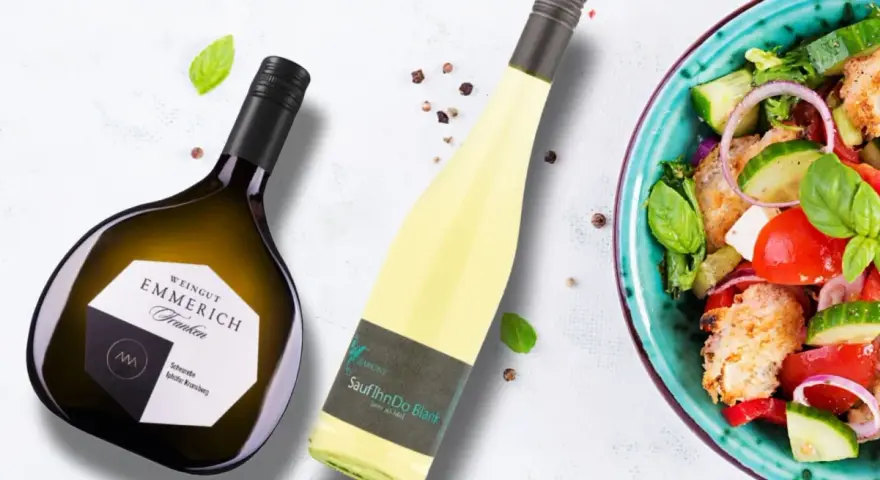 Zwei Flaschen Wein, eine davon eine Scheurebe mit fruchtigem Geschmack, neben einem frischen Salat.