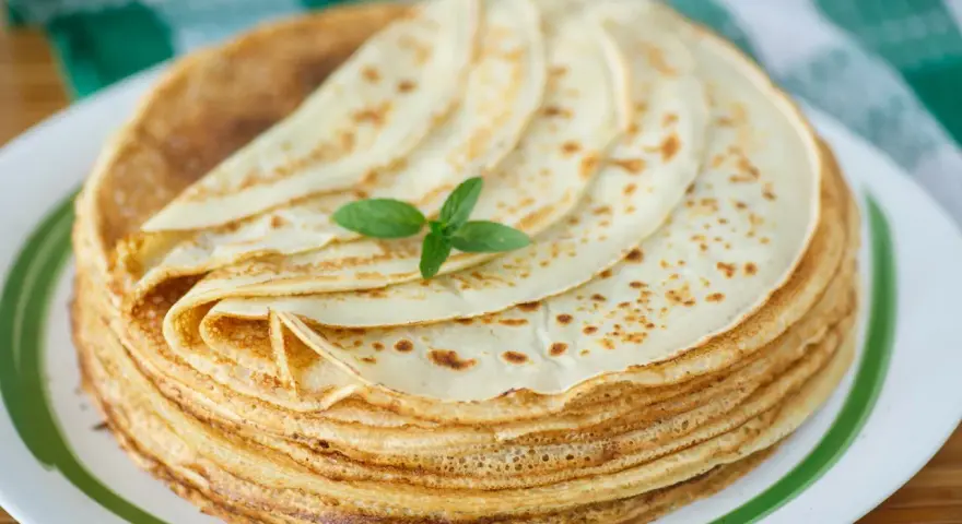 Ein Stapel goldbrauner Pfannkuchen, wie nach Omas Pfannkuchen Rezept, mit einem Minzblatt garniert.