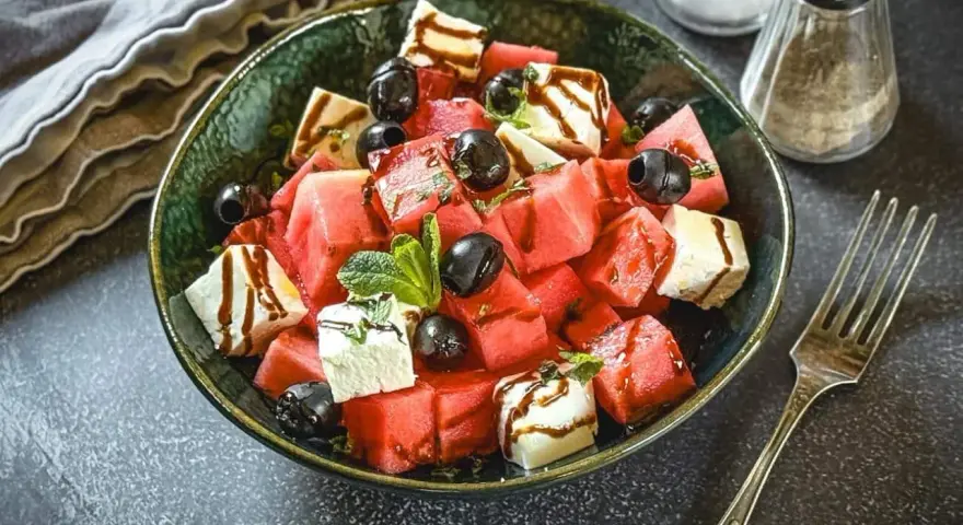 Erfrischender Melone Feta Salat mit schwarzen Oliven und Minze, beträufelt mit Balsamico-Glasur.
