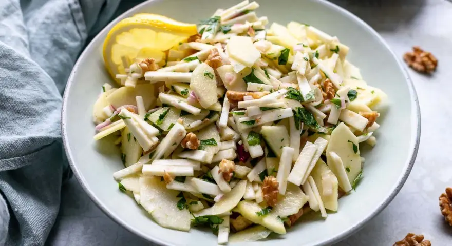 Frischer sellerie salat mit Äpfeln, Walnüssen und Kräutern, garniert mit einer Zitronenspalte.
